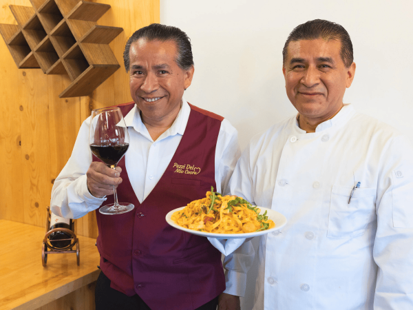 Teodulo and Gaspar Mauricio, owners, holding a class of wine and plate of pasta. 